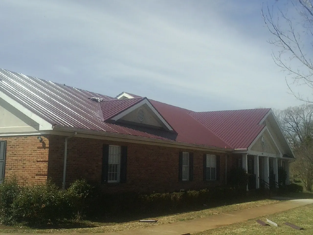 Red metal roof with gabled entries on a long brick building, from a Hail Damage Roof Repair job in Kamiah