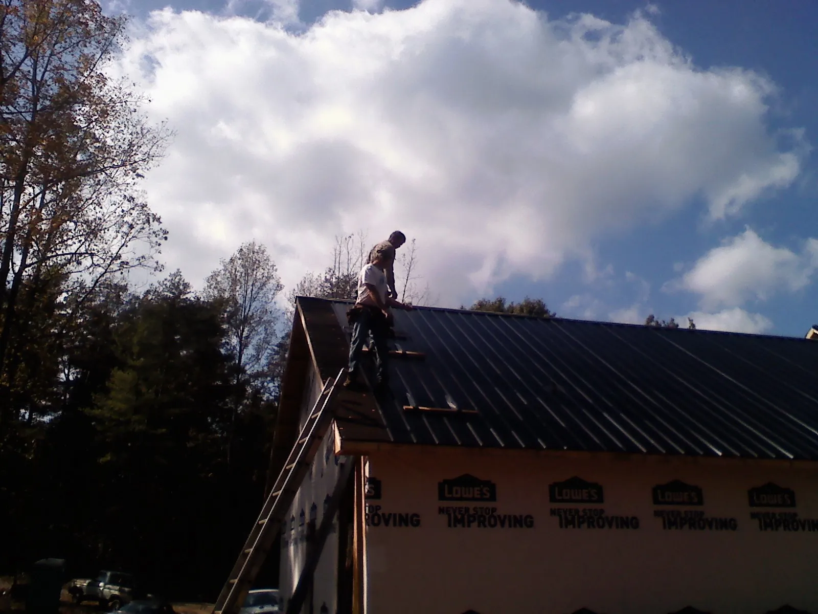 Roofer fastening dark metal panels high against a cloudy sky, from a Roof Inspection job in Kamiah