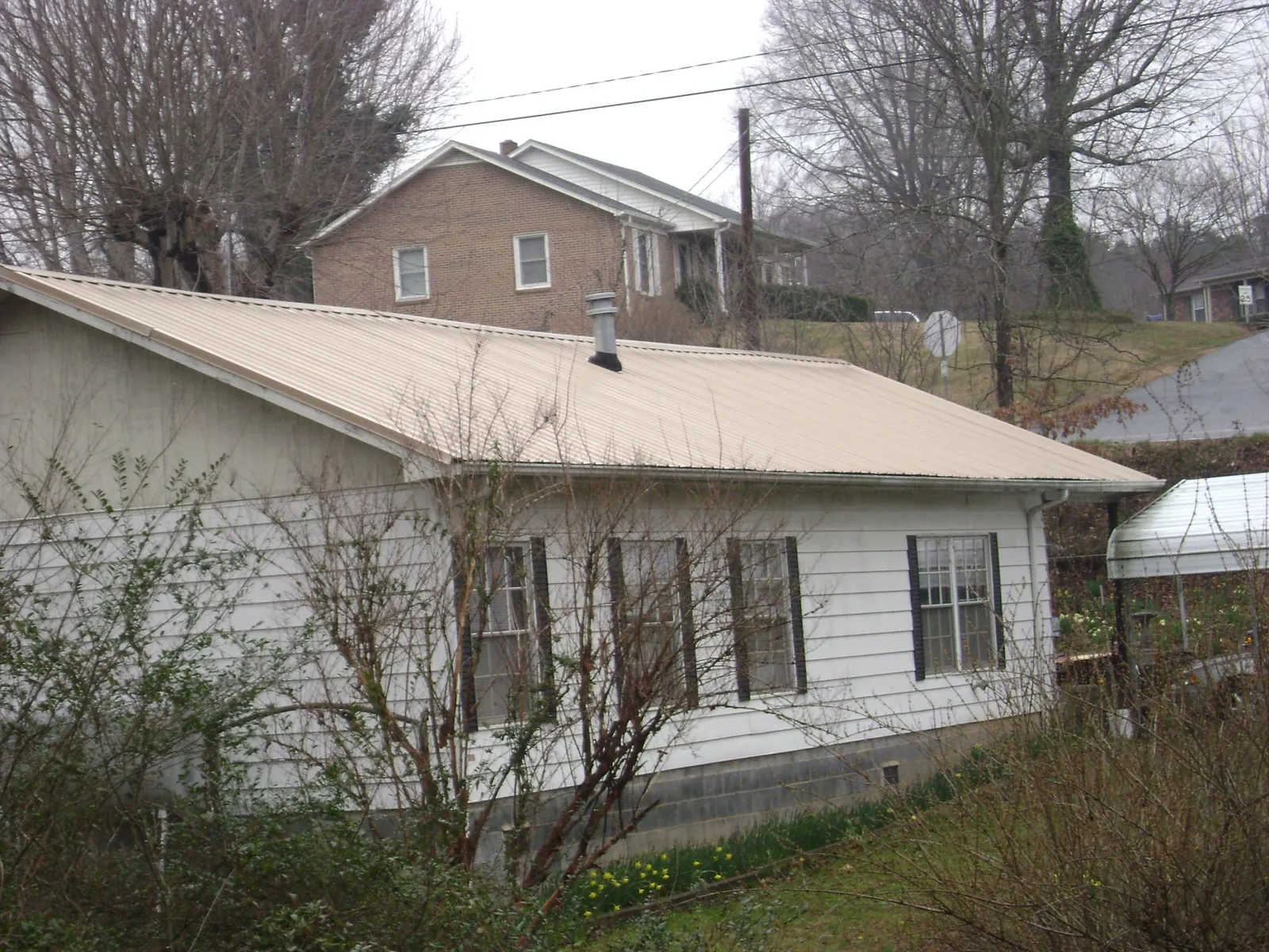 Tan metal roof on a white sided house set into a hillside — Commercial Roofing by Roofing Brothers in Kamiah